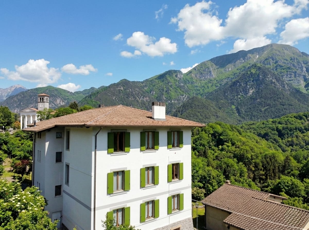 L'edificio delle ex scuole di Pielungo, oggi appartamenti in affitto in Val d'Arzino, con le montagne sullo sfondo