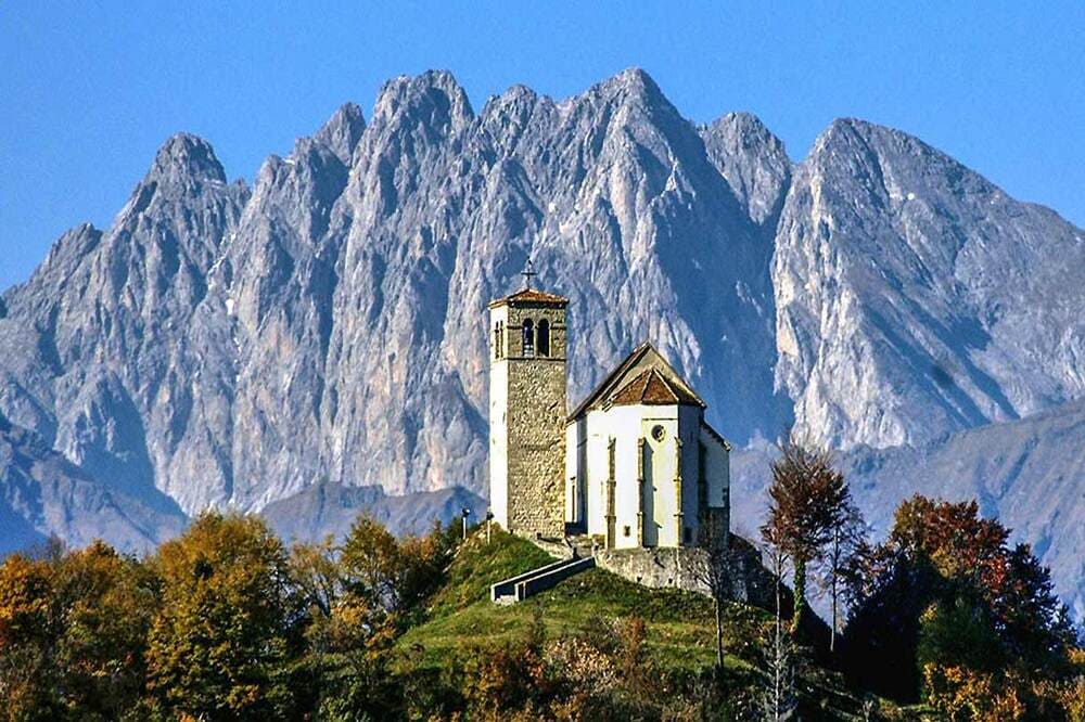 Chiesa storica in Carnia con montagne alpine sullo sfondo, patrimonio culturale e religioso del Friuli Venezia Giulia