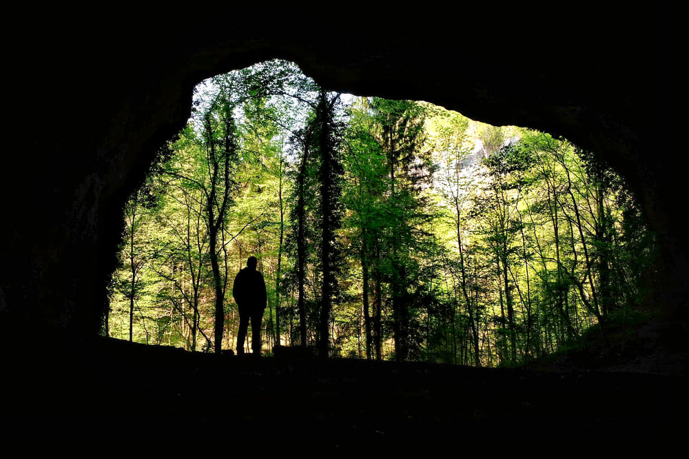 Buse dai Pagans nella Forra della Cjanevate, con luce naturale che penetra e silhouette di una persona, creando un'atmosfera suggestiva.