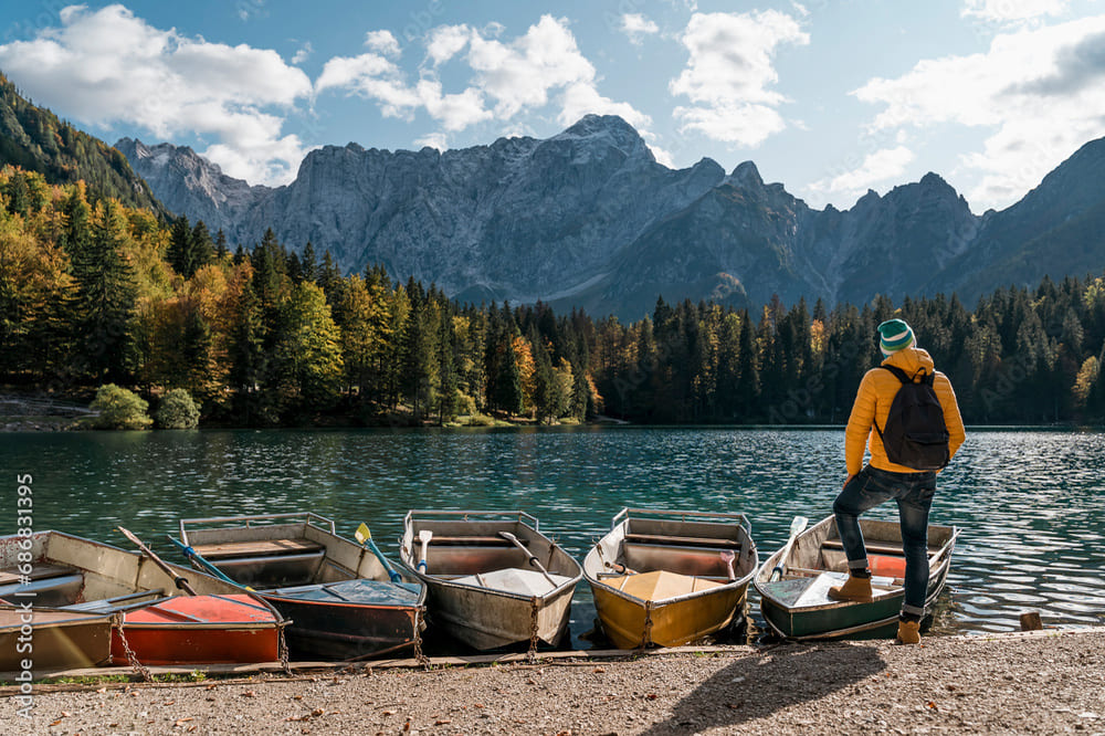 Uomo osserva barche sul Lago di Fusine Inferiore in autunno