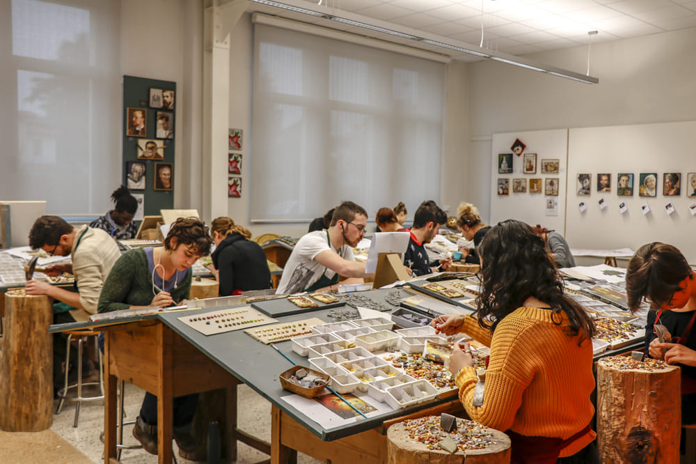 Interni della Scuola Mosaicisti del Friuli, mostrando studenti al lavoro sui loro progetti di mosaico in un ambiente luminoso e ispiratore.