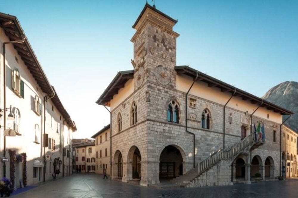 Facciata del Palazzo Comunale di Venzone in stile gotico-veneziano, con un ampio porticato e una torretta angolare con orologio, situato nella piazza centrale.