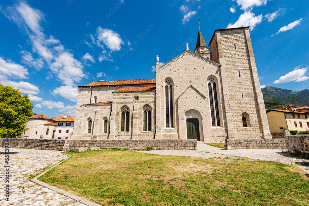 Esterno del Duomo di Sant'Andrea a Venzone, con la sua facciata romanica e la grande porta d'ingresso, immerso nel contesto urbano storico.