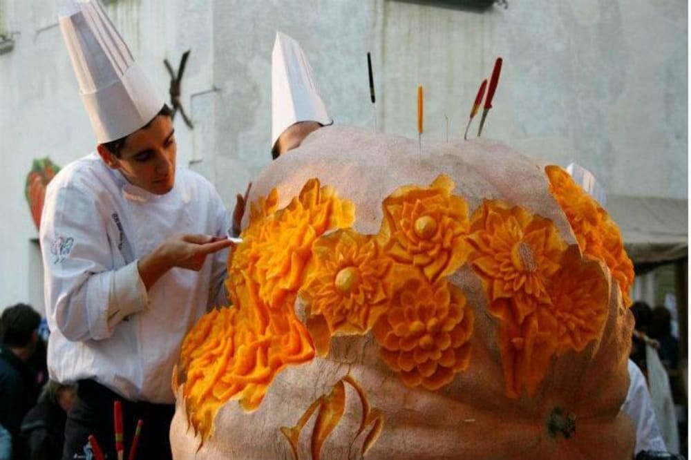 Scena vivace della Festa della Zucca a Venzone, con bancarelle colorate, zucche artisticamente decorate e persone in costume medievale.